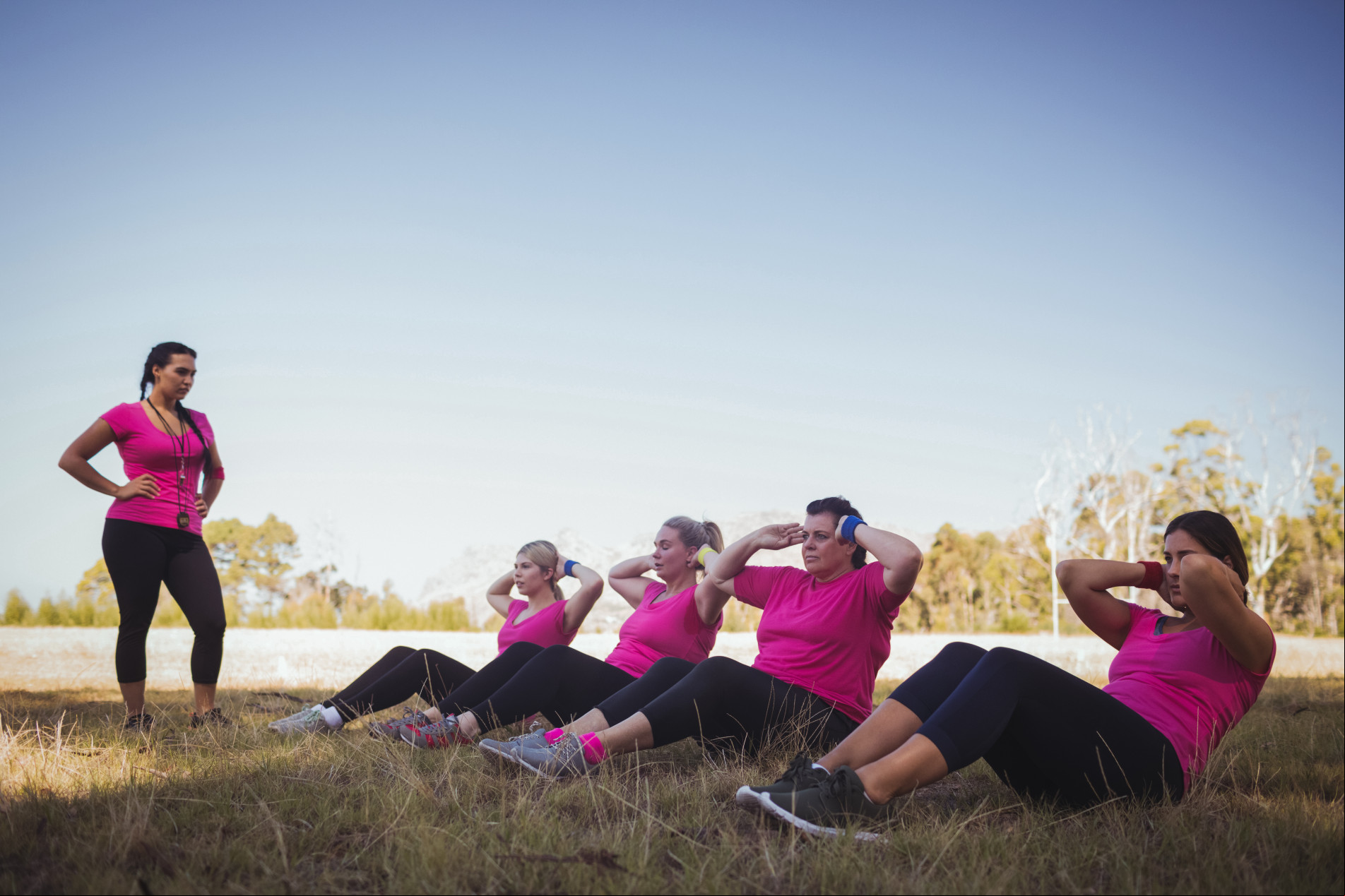 Female trainer instructing women while exercising in the boot camp on a sunny day
Local